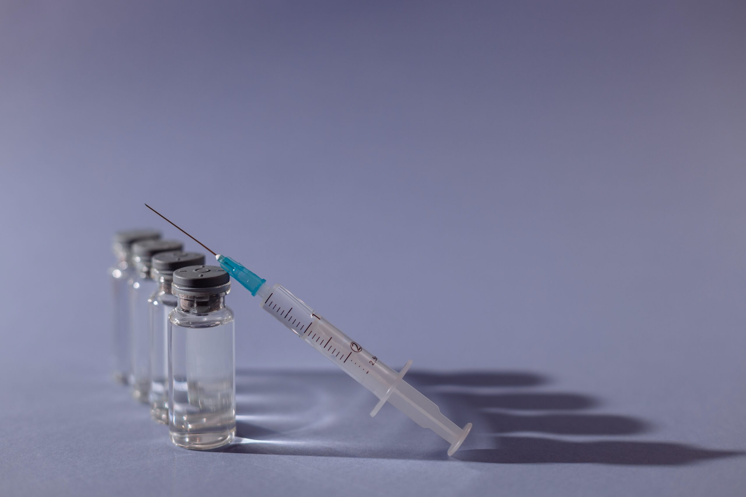 Injekční stříkačka s jehlou opřená o čtyři skleněné lahvičky s očkovací látkou