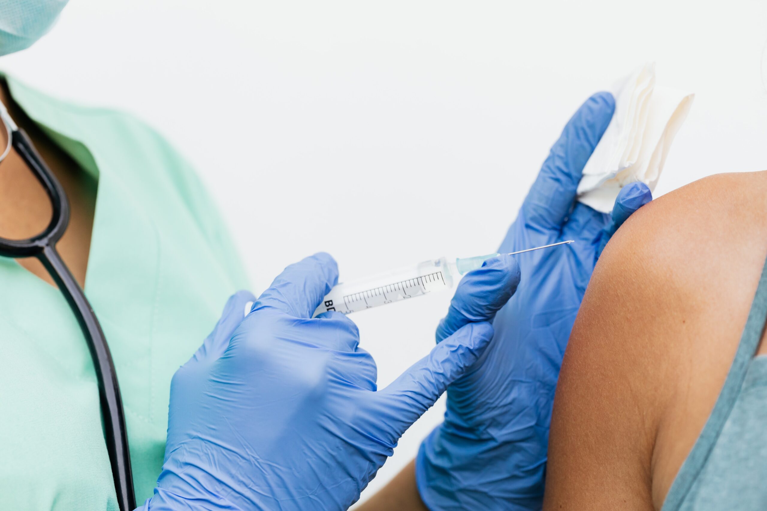 Lékařka aplikuje mladému člověku očkovací látku do ramene pomocí injekční stříkačky s jehlou